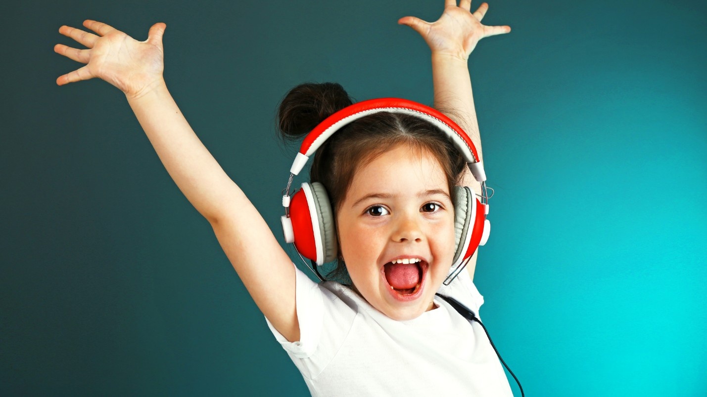 A child wearing headphones looking happy with arms raised up.