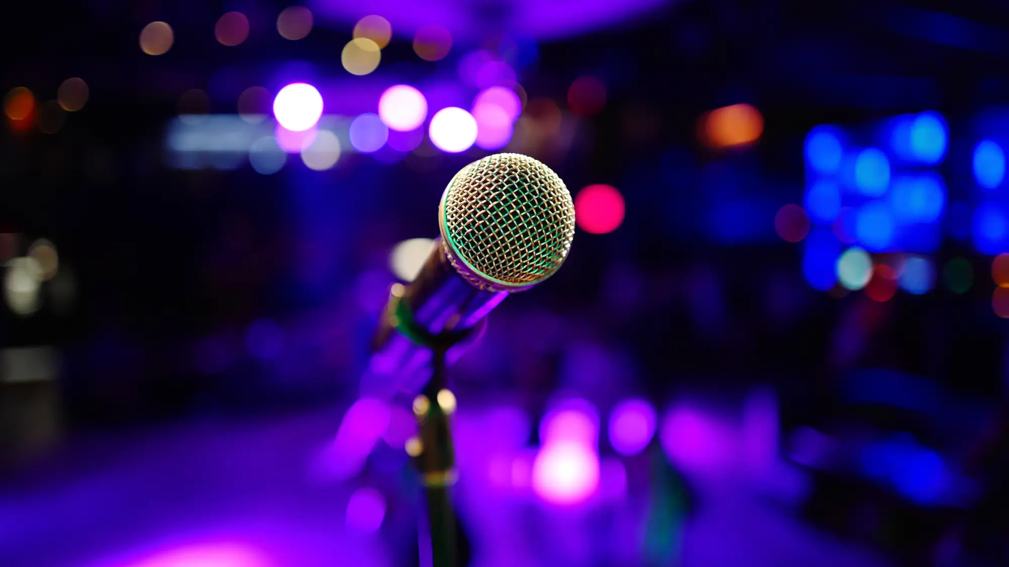 A microphone on a mic stand at a venue with blue and purple lighting.
