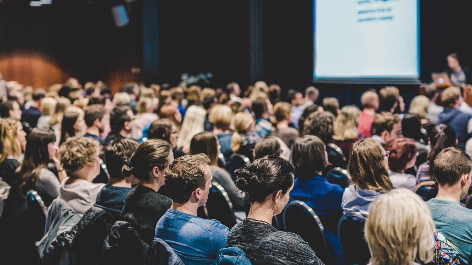 A large group of attendees at a corporate event where a presenter is speaking.