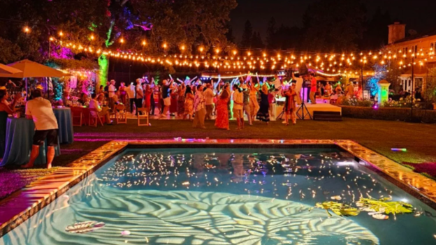 A large wedding reception with multiple layers of lighting across the outdoor venue.