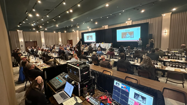 A ballroom set up for a large corporate event with screens set against black drapes.