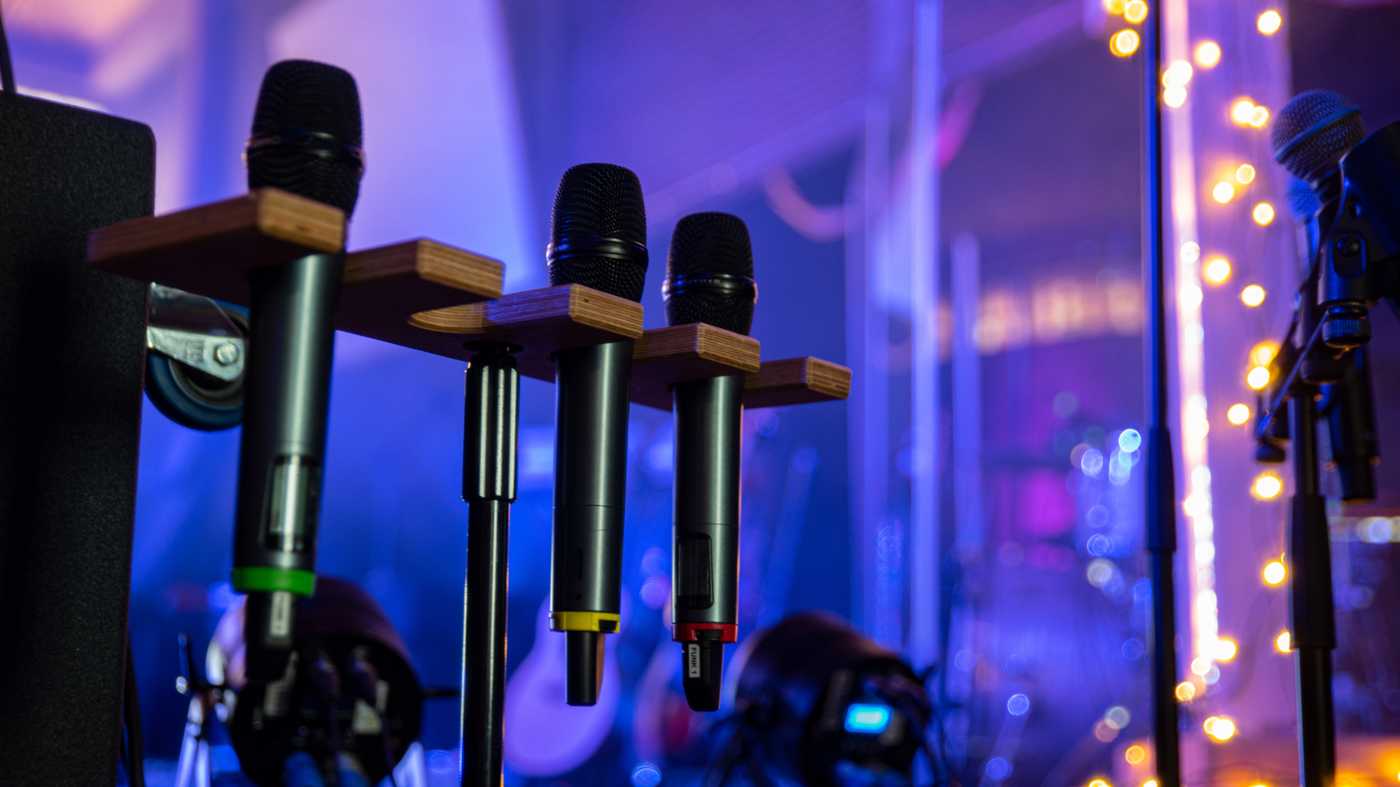 Three cordless microphones held on a wooden stand in front of other AV equipment.